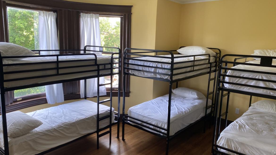 Three bunkbeds in a sun-filled room with yellow walls and wood floors.